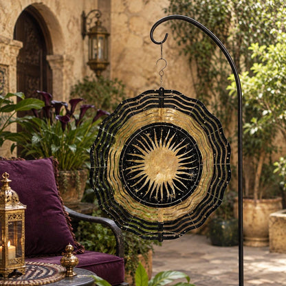 May include: A circular metal wind spinner featuring a black and gold sun design with radiating rays and small star accents. The spinner has a scalloped, wavy edge and is suspended from a black metal hook, displaying a celestial pattern.