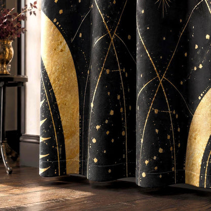 May include: A black curtain featuring a gold celestial pattern with large crescent shapes, thin intersecting lines, and scattered gold speckles. The fabric hangs in vertical folds, displaying a dark background with metallic gold accents.