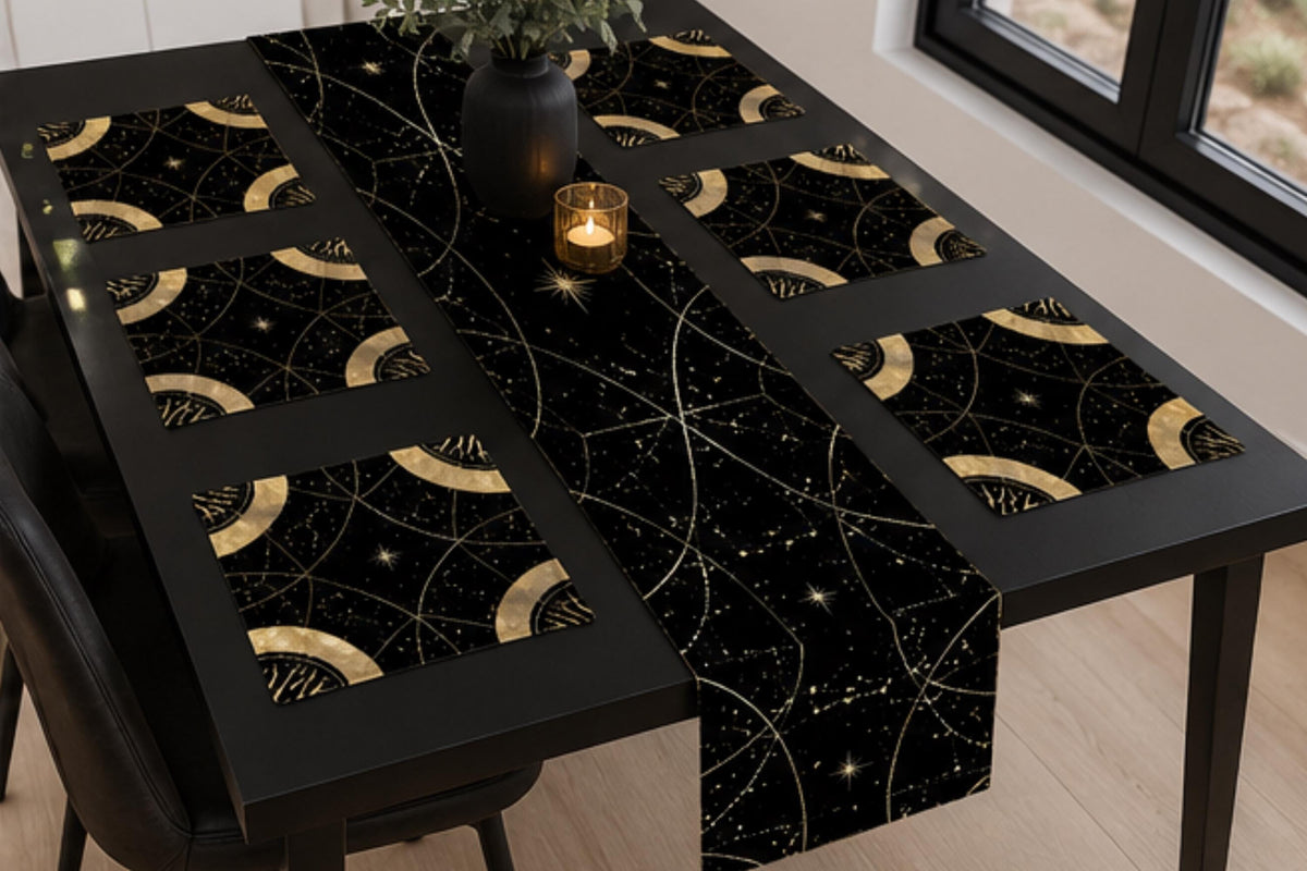 May include: A black table runner and four matching square placemats featuring a gold celestial pattern of interconnected circles, thin lines, and small stars. The set is arranged on a black dining table with a dark vase and a small candle.